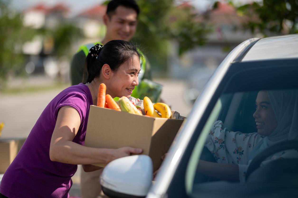 Woman delivering food bank groceries to a car.